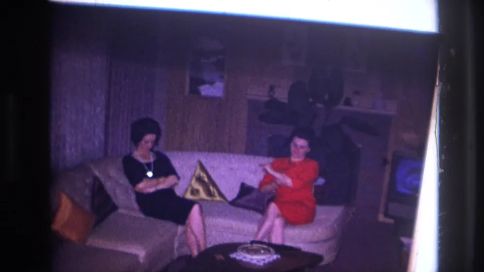 Two adult women sit on a white couch in an Ottawa home interior, one in a black dress and one in a red dress holding papers.