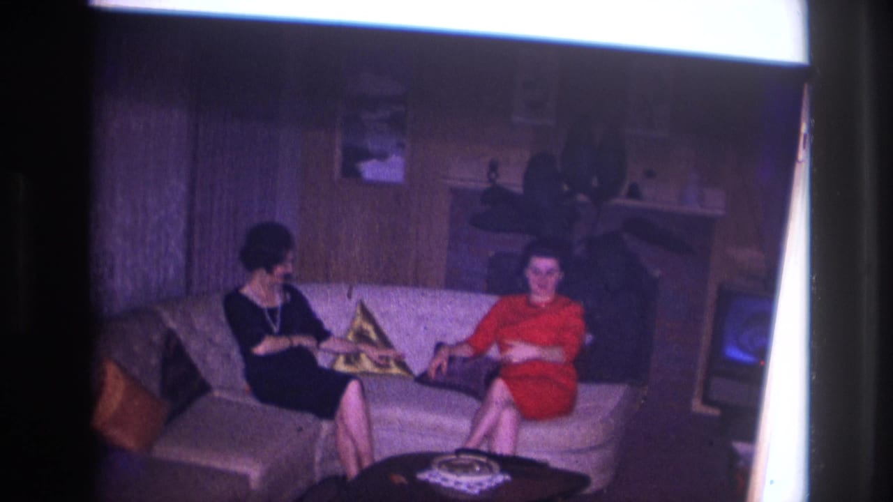 Two women converse on a sofa, with one turned toward the other beside patterned pillows.