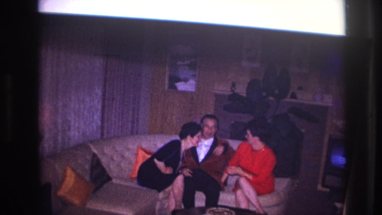 Three adults sit close together on a sofa in a dim living room.