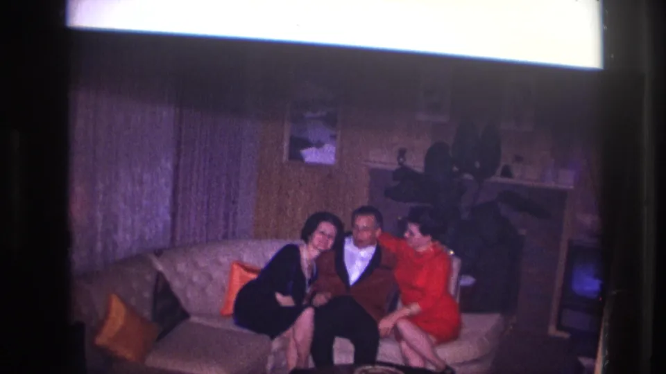 Two women in dark and red dresses lean affectionately toward a man in a suit on a sofa in the Ottawa interior.