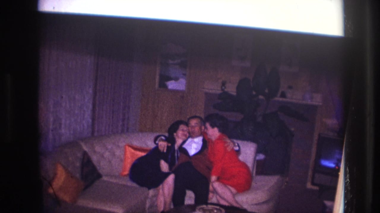 Two women sit on either side of a man on a couch, leaning close to his face.