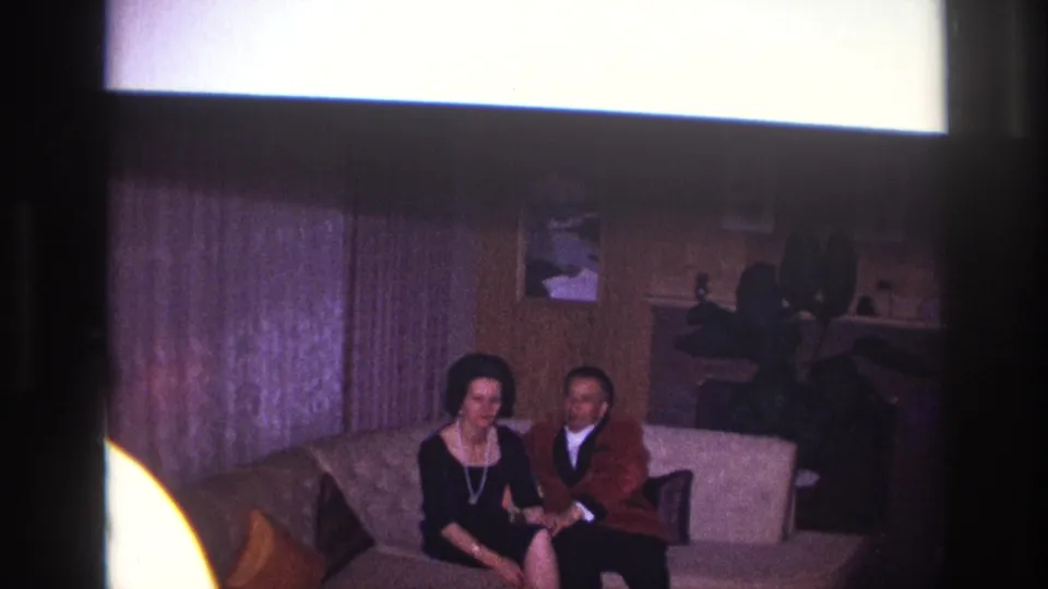 A woman in a black dress and a man in a brown jacket sit on a light couch in a softly lit Ottawa living room.