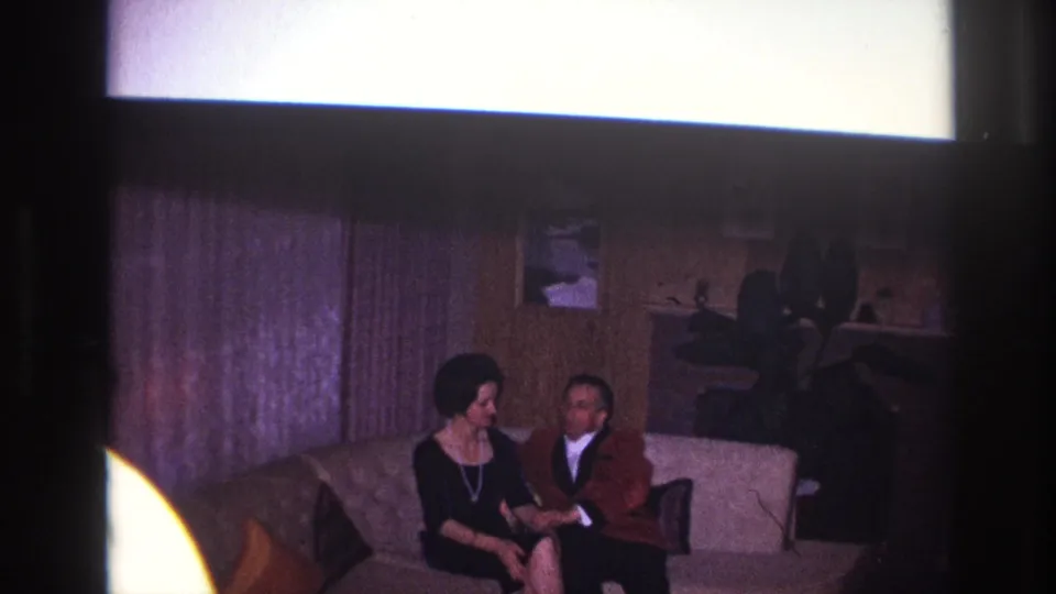 In the closing frame, a man and woman sit close on a couch in a 1967 Ottawa home interior with curtains and wall decor behind them.