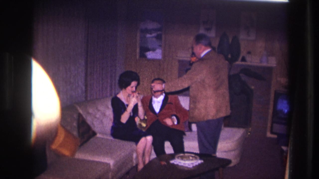 A man lights a seated man's cigarette while a woman sits beside him on a sofa.