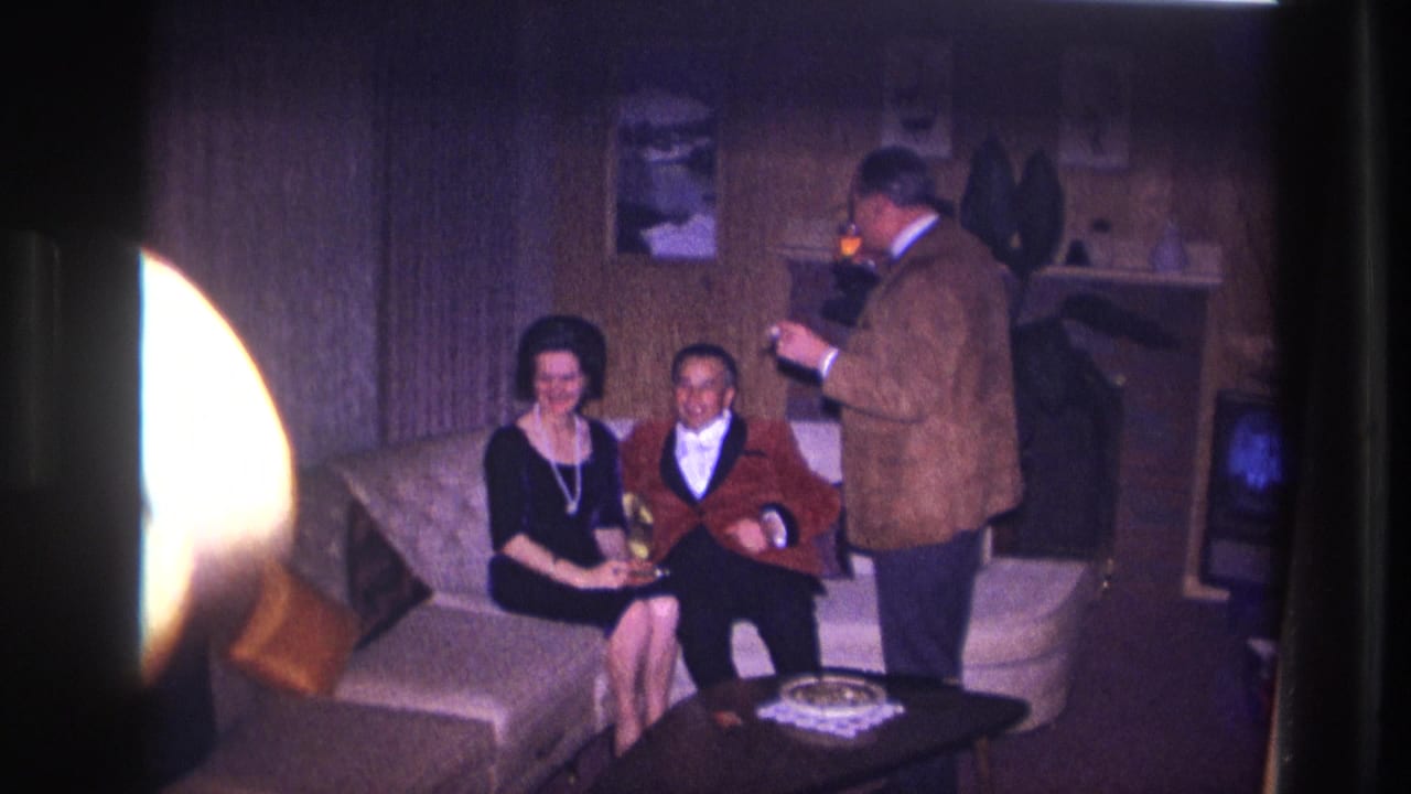 1967 Ottawa home-movie frame showing three adults socializing with drinks in a wood-paneled living room.