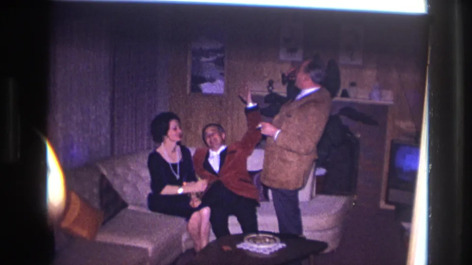 1967 Ottawa home-movie frame showing a playful toast or exchange between adults in a living room.