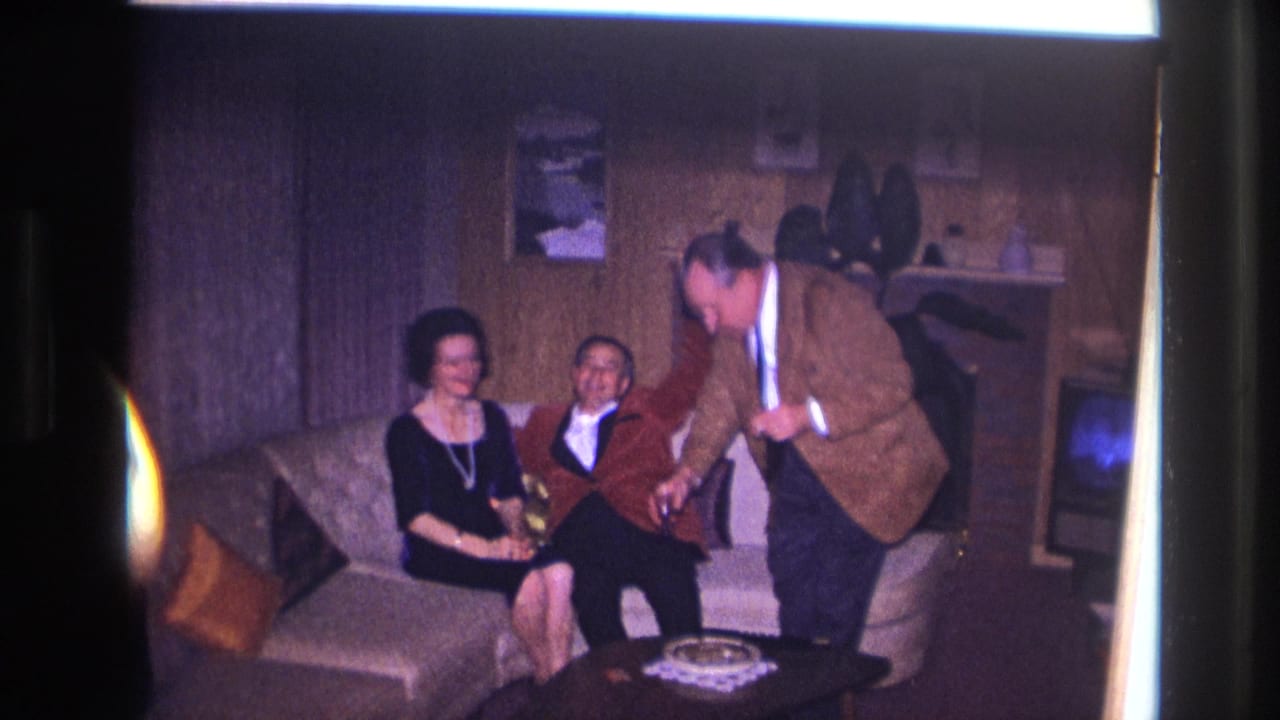 Three adults in a living room as one man leans toward a coffee table with drinks.