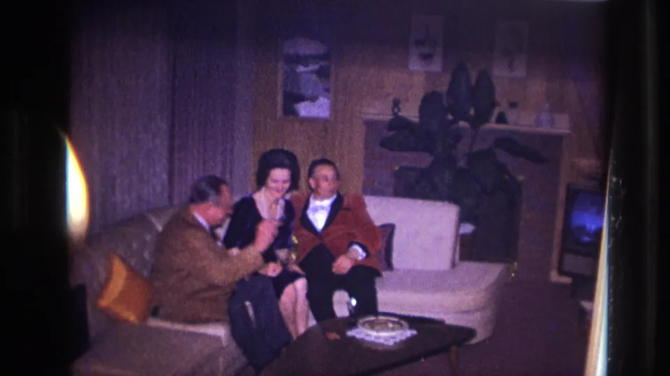 1967 Ottawa home-movie frame showing three adults seated together on a couch during a living-room conversation.