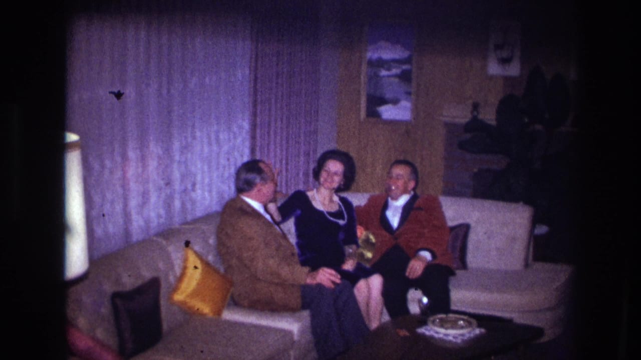 1967 Ottawa home-movie frame showing two men and a woman seated on a beige couch in a private living room.