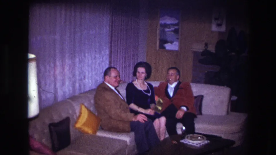 1967 Ottawa home-movie frame of three adults seated on a couch, with a low table and ashtray in the foreground.