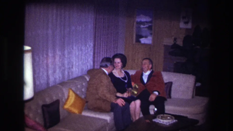 1967 Ottawa home-movie frame showing a man leaning toward a woman as another man sits beside them in a private living room.