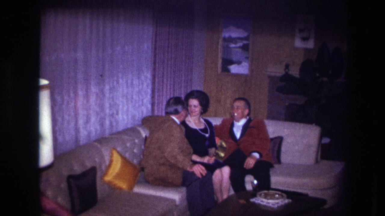 Ottawa 1967 home-movie frame showing two men and one woman seated close together on a sofa in a private living room.