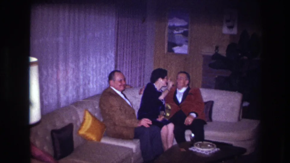 Ottawa 1967 home-movie frame showing a woman between two men on a sofa, with a coffee table and living-room decor nearby.