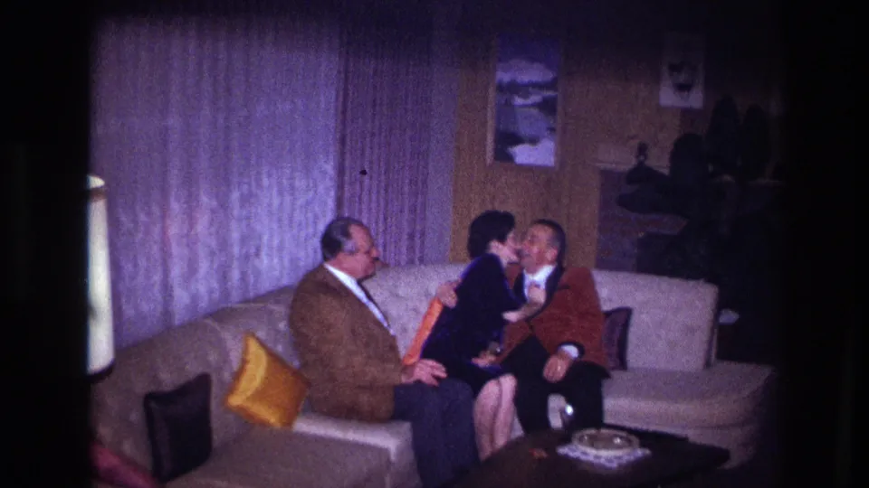 Ottawa 1967 frame showing an affectionate greeting or kiss between adults on a sofa in a private living room.