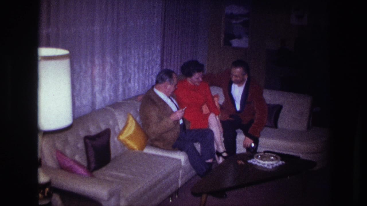 Three adults seated on a pale sectional couch in a living room.