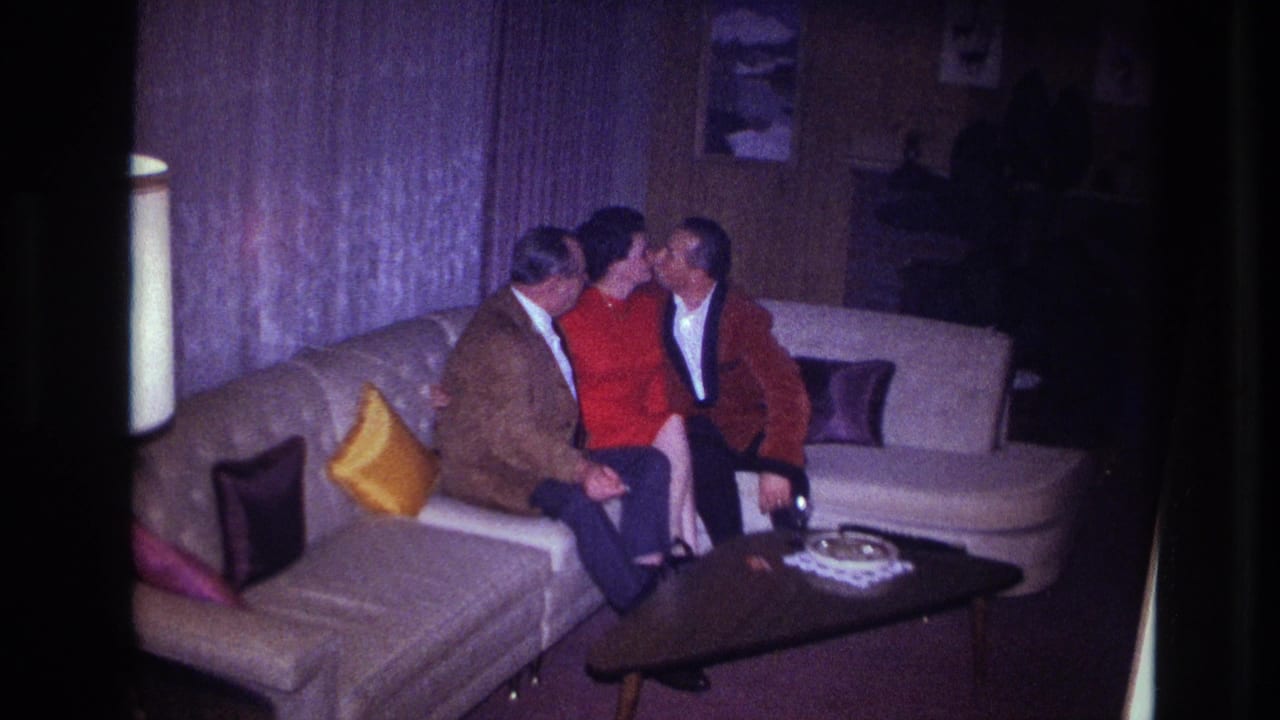 A woman in a red dress sits between two men on a sectional couch in a 1967 Ottawa home interior.