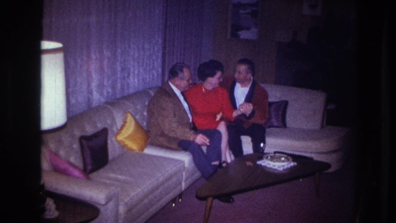 Woman in red turns toward a man in a red cardigan while another man sits beside her.
