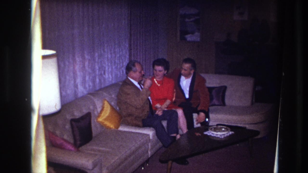 A seated man reaches toward a woman in red while another man sits beside her.