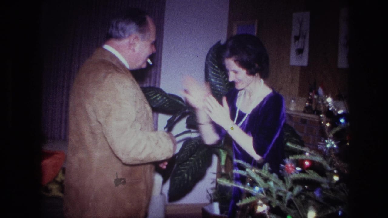 Man and woman clap facing each other beside a decorated Christmas tree in a living room.
