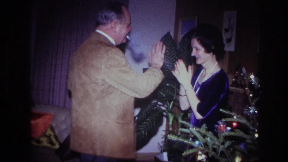 A 1967 Ottawa frame shows two adults raising their hands together during a playful holiday dance in a living-room interior.