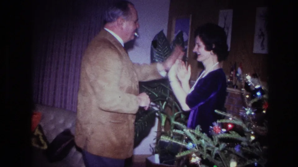 The final frame shows the couple facing each other, hands raised in rhythm, beside a lit Christmas tree in the Ottawa home interior.