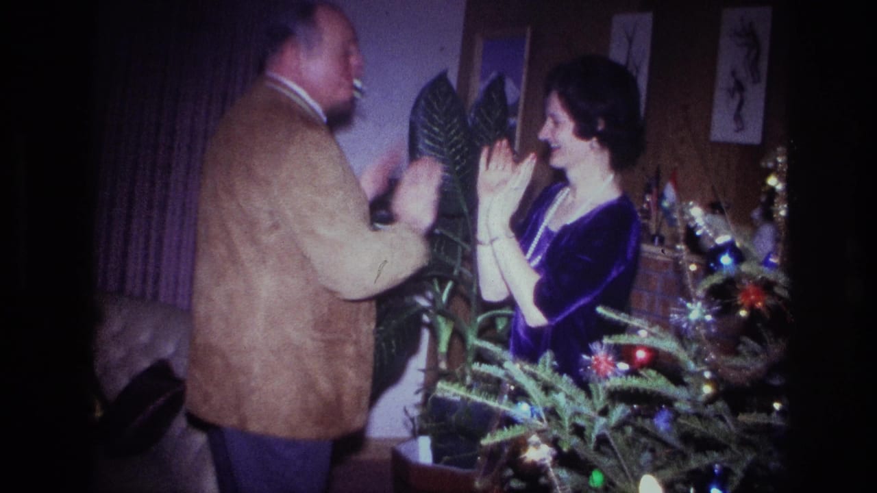 In a 1967 Ottawa home-movie frame, a man in a brown jacket and a woman in a purple dress face each other beside a Christmas tree.