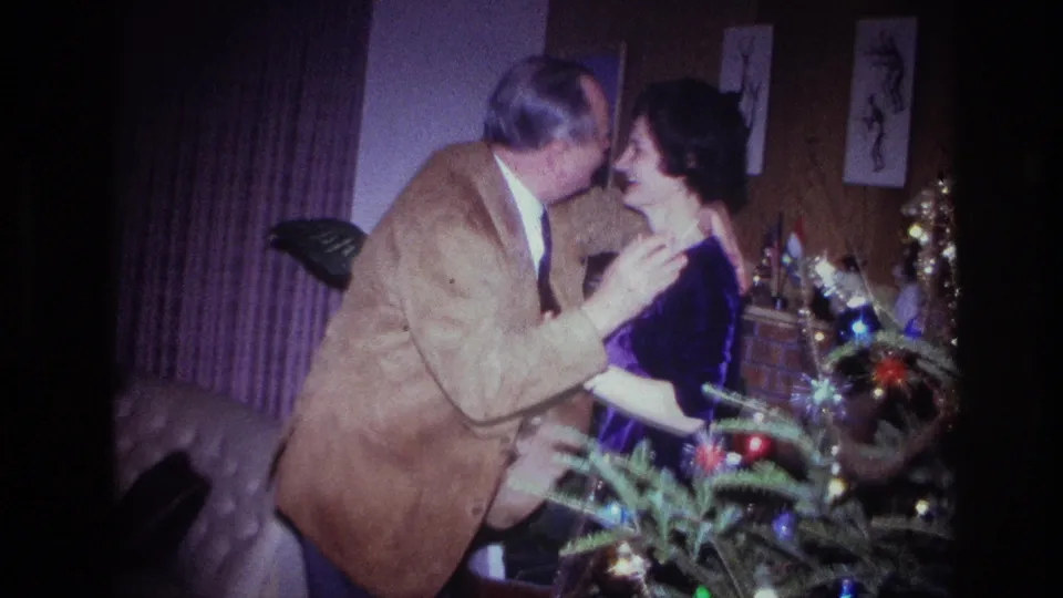 In the Ottawa Christmas party footage, the man leans in to kiss the woman while she stands beside the tree in a purple dress.