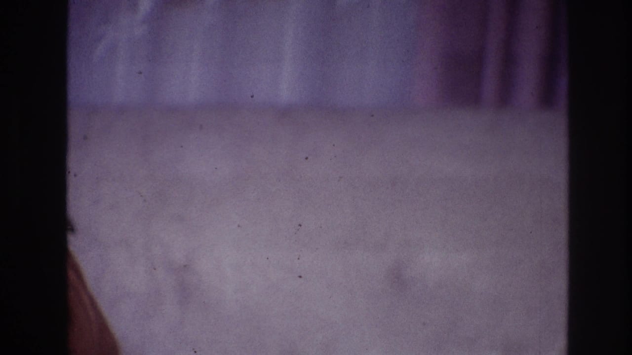 1967 Ottawa home-movie frame showing purple carpet, draped curtain, film borders, and a partial arm near the left edge.