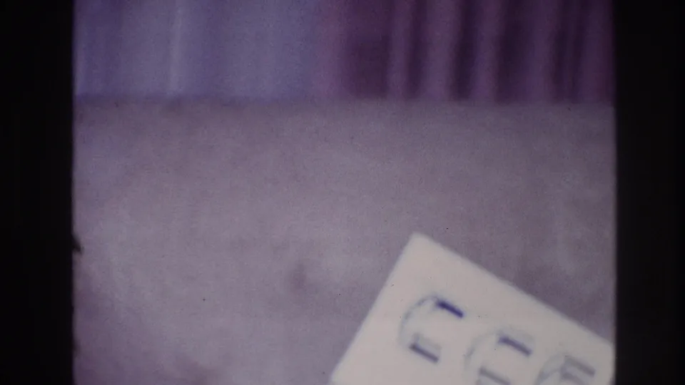 1967 Ottawa home-movie frame with a white paper bearing blue symbols on purple carpet beside dark film-frame borders.