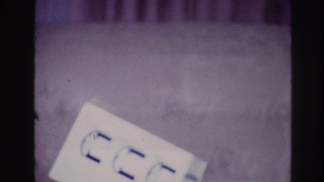 1967 Ottawa close-up showing a white paper with blue markings against a purple carpet in grainy 8mm home-movie footage.