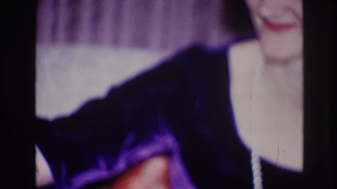 Smiling woman in a dark top, partly cropped, seated indoors near curtains.