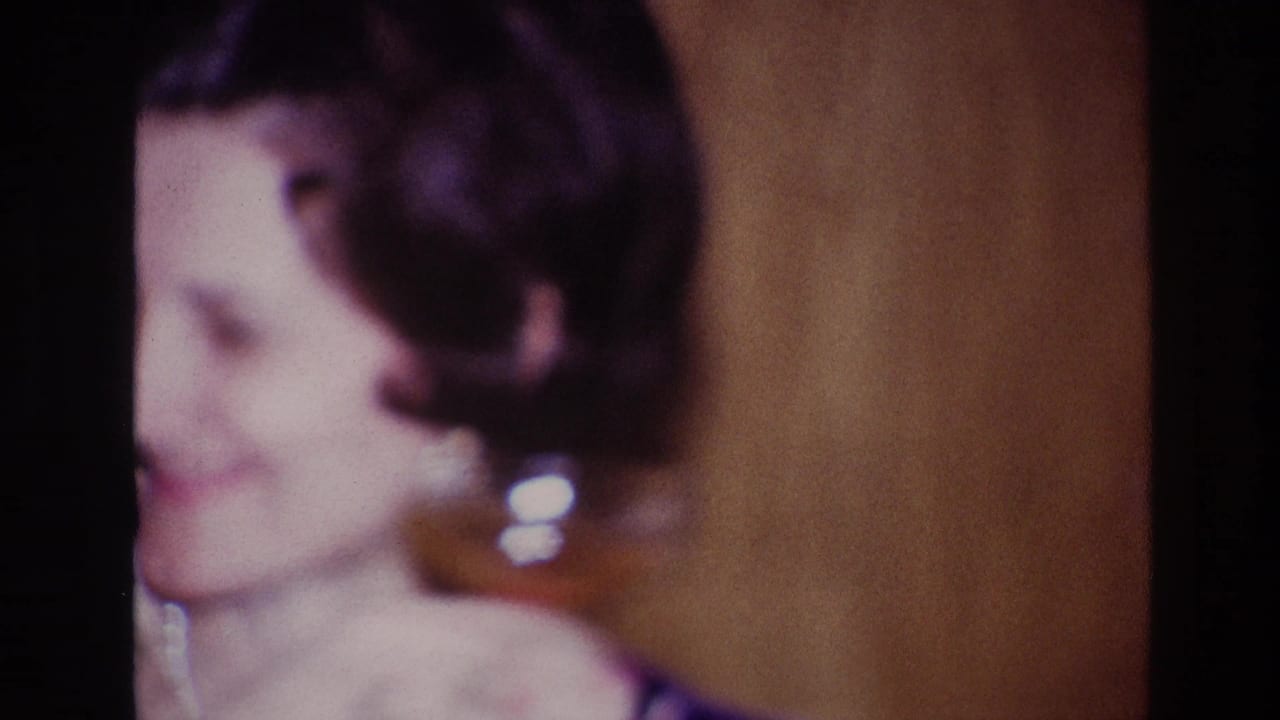 Soft 1967 Ottawa 8mm close-up of a woman with short dark hair, earrings and a pearl necklace in a warm indoor setting.