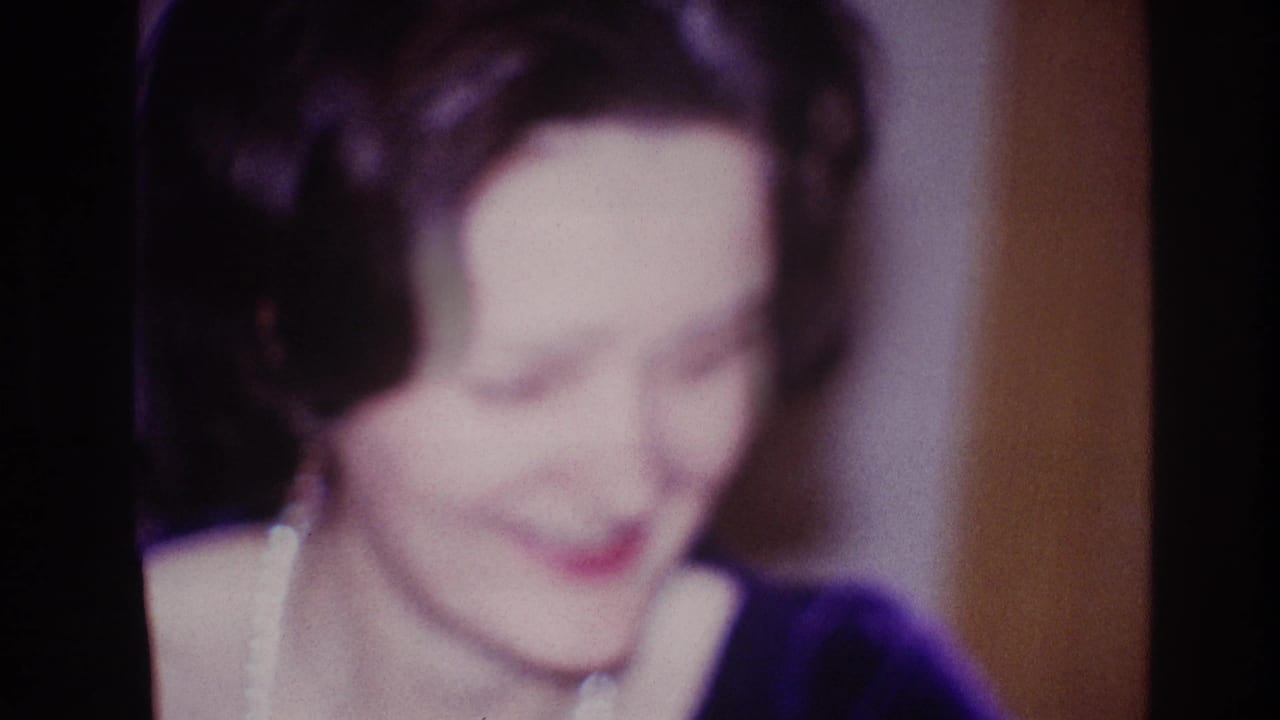 Soft 1967 Ottawa close-up of the woman smiling downward, with pearl necklace and dark dress visible in a warm interior.