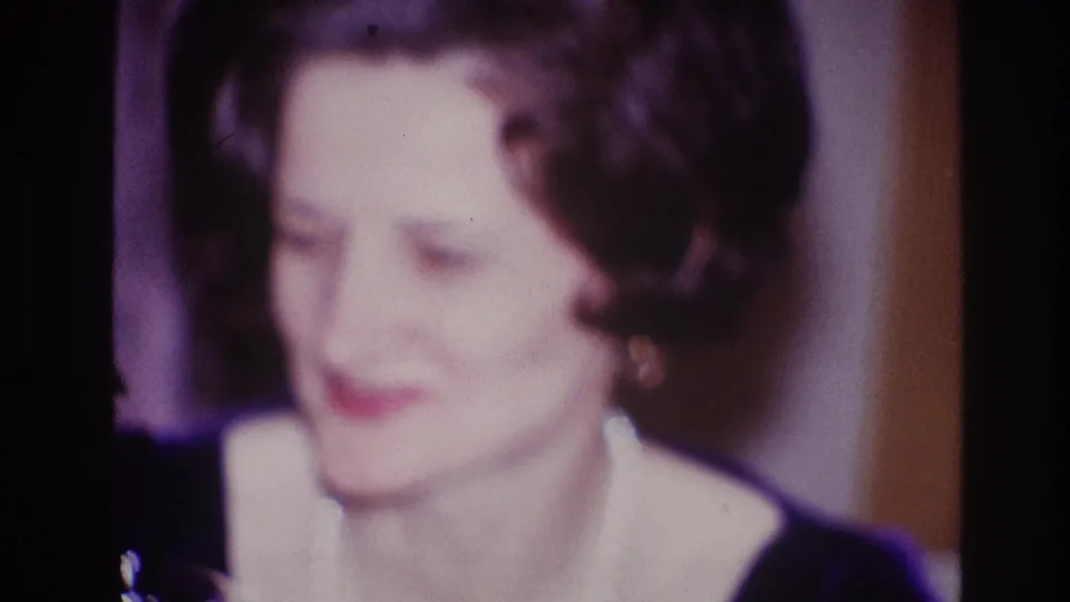 Older woman in Ottawa 1967 home-movie footage smiles softly, wearing red lipstick, earrings, and a pearl necklace.