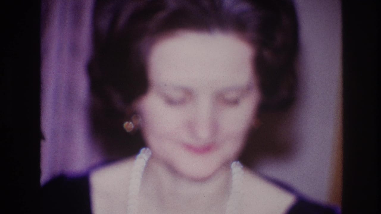 The woman looks down in the 1967 Ottawa home-movie frame, her pearl necklace and earrings visible in soft focus.