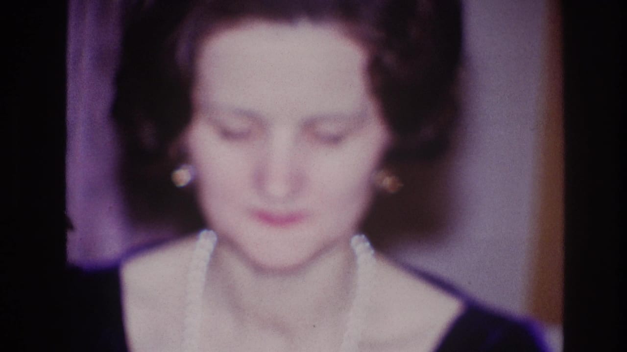 Soft-focus woman looking down with pearl necklace and earrings in an interior room.
