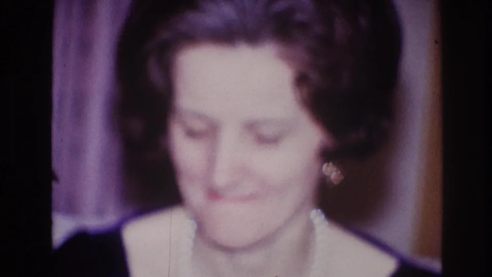 A woman in pearl jewelry appears to purse her lips while seated or standing in a private Ottawa interior in 1967 footage.