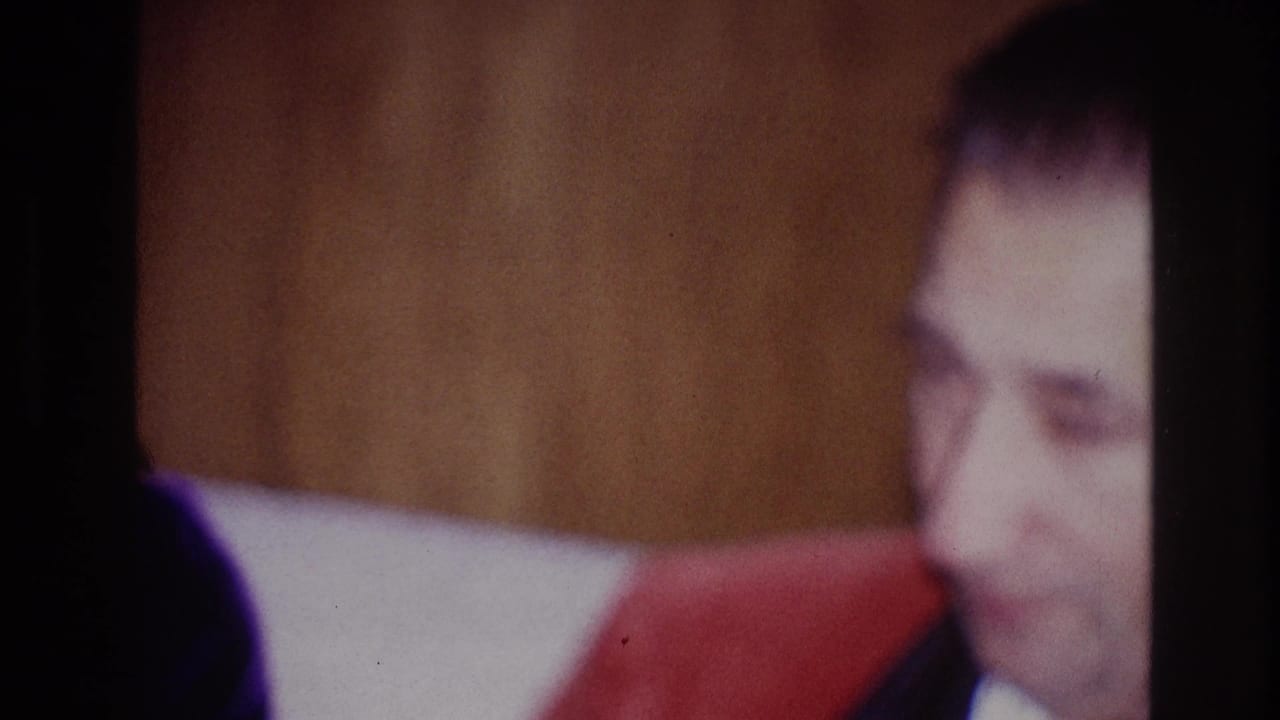 A man appears at the right edge of the 1967 Ottawa home-movie frame, wearing dark clothing near a private interior wall.