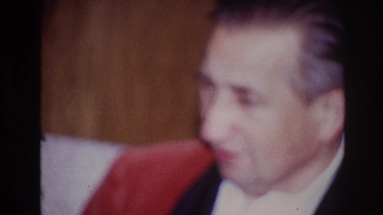 Soft-focused man in a red jacket seated on a couch indoors.