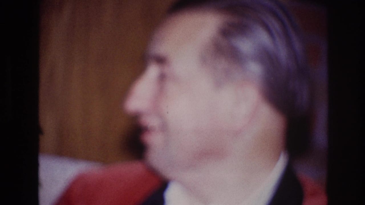 Profile view of the seated man in formal clothing, filmed inside an Ottawa home in 1967.