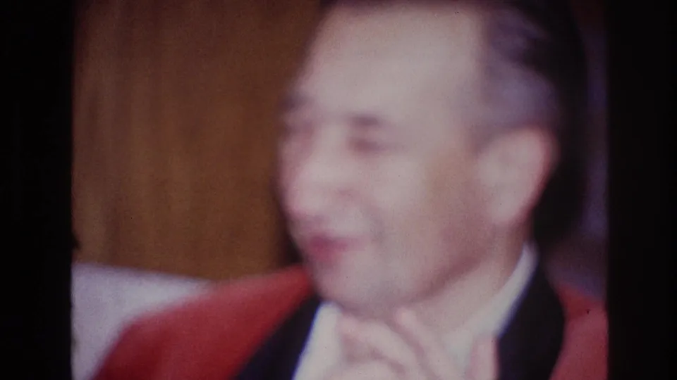 1967 Ottawa 8mm frame showing a smiling adult man in a red jacket and white shirt inside a warm-lit room.