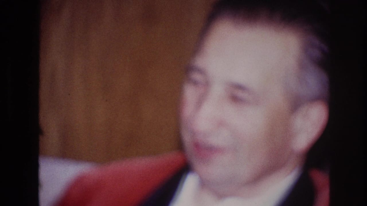 Man in a red jacket smiling in soft indoor light.