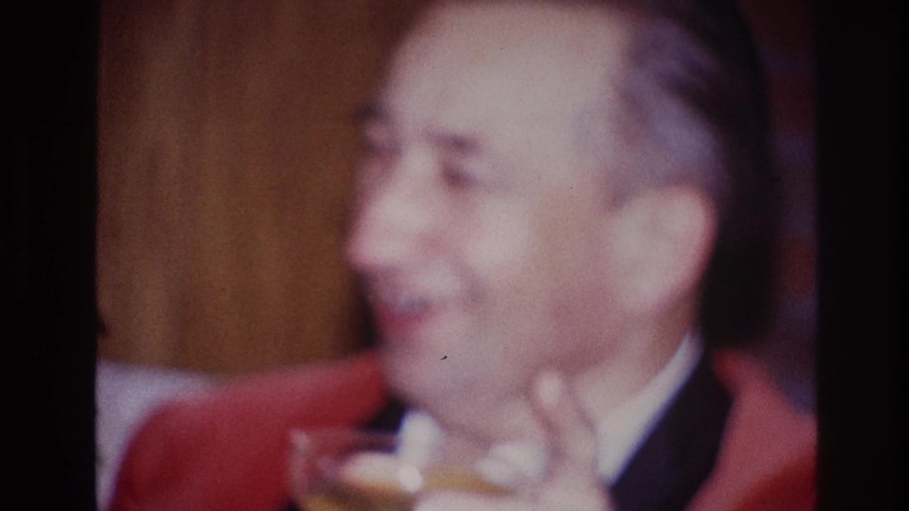 An older man in a red jacket and white shirt smiles in a private Ottawa interior as his drink drops lower in frame.