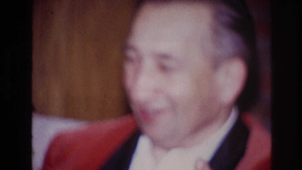 The Ottawa home-movie shot ends on the older man smiling broadly in formal clothing against a warm wood-paneled interior.