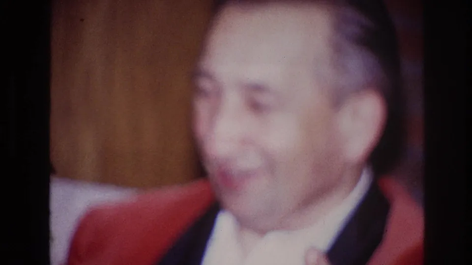 The Ottawa home-movie shot ends on the older man smiling broadly in formal clothing against a warm wood-paneled interior.
