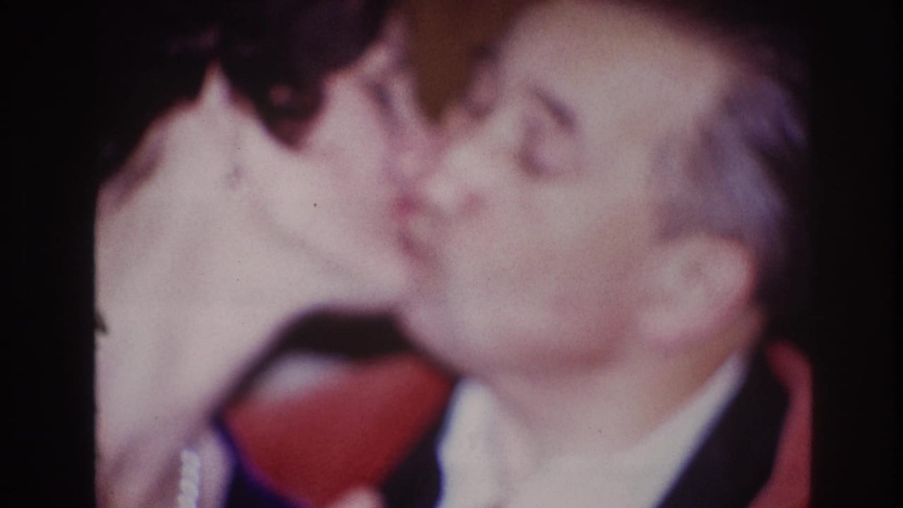 A dark-haired woman wearing pearls leans in to kiss the seated man during the 1967 Ottawa home-movie clip.