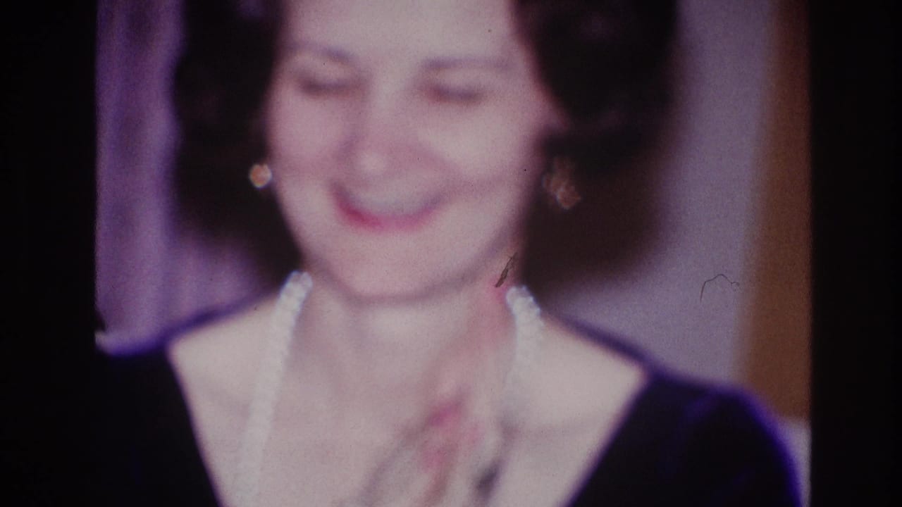 Woman in pearls smiling and clapping in a softly lit stage setting.