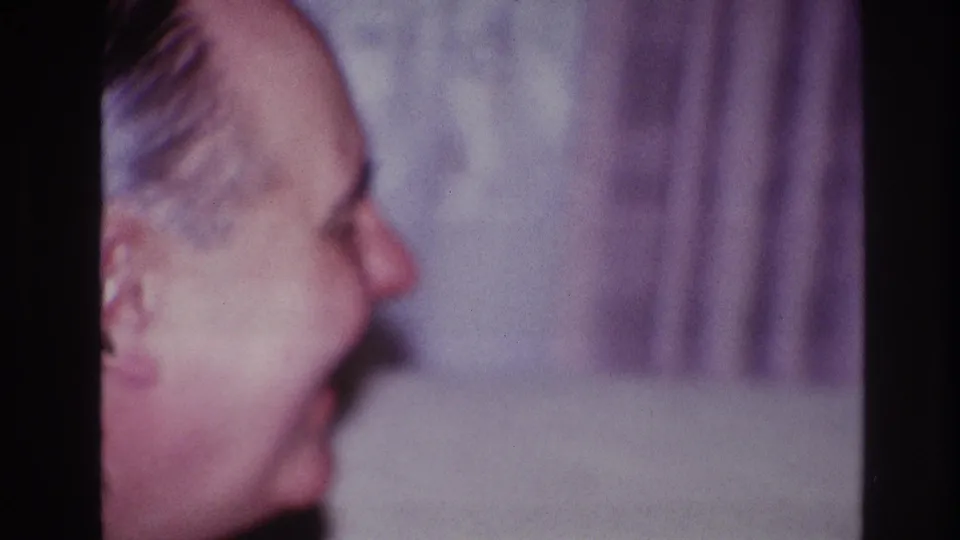In 1967 Ottawa home-movie footage, an older man is seen in soft side profile smiling near a pale curtain.