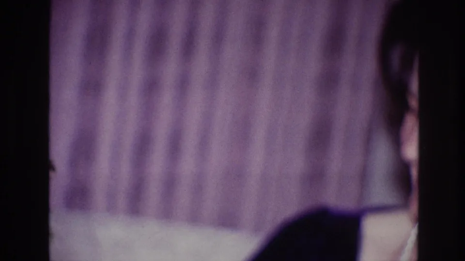 Soft Ottawa 1967 8mm frame with the woman partly cropped at the edge, dark clothing visible against the curtain backdrop.