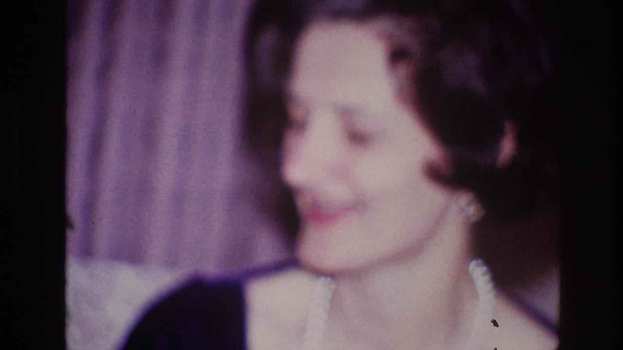 Woman in pearls turns to the side and smiles in a softly focused interior shot.